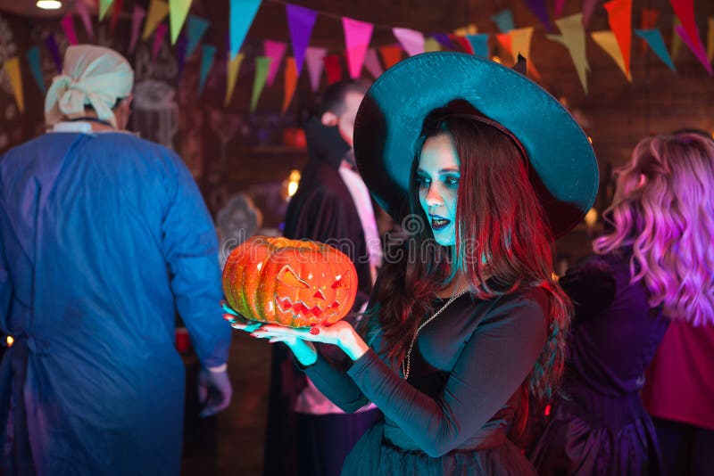 Portrait of young witch looking shocked at her punmpkin for halloween celebration. Woman with a big witch hat. Portrait of young witch looking shocked at her punmpkin for halloween celebration. Woman with a big witch hat.