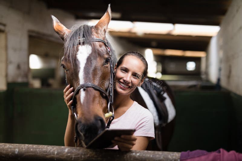 Portrait de jockey féminin tenant la tablette tout en se tenant prêt le cheval photo stock Portrait de jockey féminin tenant la tablette tout en se tenant prêt le cheval photo stock