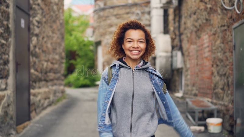 Portrait de l'adolescent heureux d'Afro-américain marchant et dansant dans la rue regardant alors l'appareil-photo et le sourire banque de vidéos