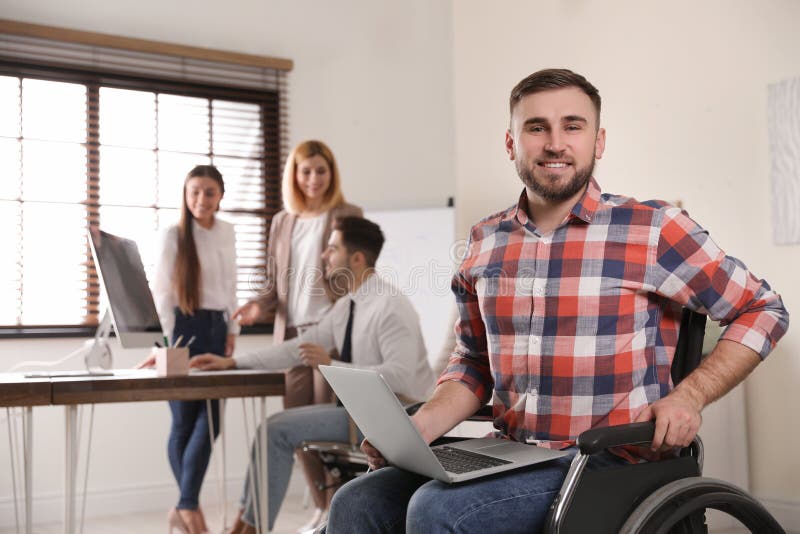 Portrait de l'homme dans le fauteuil roulant avec l'ordinateur portable et ses collègues image stock Portrait de l'homme dans le fauteuil roulant avec l'ordinateur portable et ses collègues image stock