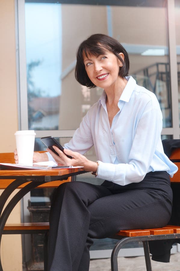 Portrait de la femme supérieure heureuse s'asseyant au café utilisant le téléphone portable photo stock