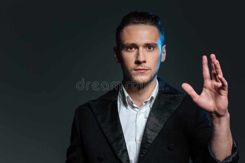Portrait de magicien sûr de jeune homme avec la main augmentée image stock Portrait de magicien sûr de jeune homme avec la main augmentée image stock