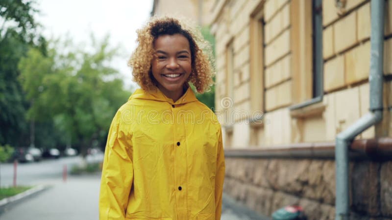 Portrait de mouvement lent de la femme de sourire d'Afro-américain dans le manteau lumineux marchant dans la rue, se tournant ver banque de vidéos