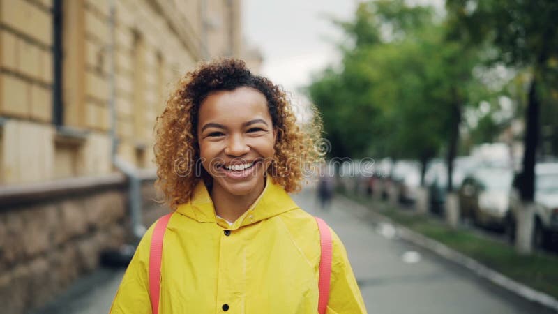 Portrait de mouvement lent de la fille heureuse d'Afro-américain souriant et regardant l'appareil-photo se tenant dehors avec les banque de vidéos