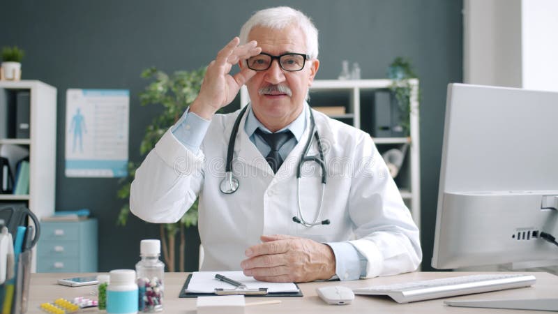 Portrait de médecin expérimenté touchant des lunettes à regarder la caméra avec le visage sérieux banque de vidéos