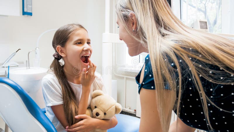 Portrait de petite fille montrant des dents à sa mère après traitement de dents dans le bureau de dentiste image stock Portrait de petite fille montrant des dents à sa mère après traitement de dents dans le bureau de dentiste image stock