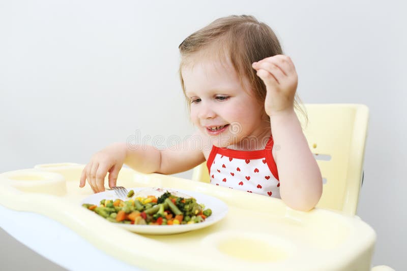 Portrait de petites 2 années heureuses de fille mangeant des poissons avec le légume images stock