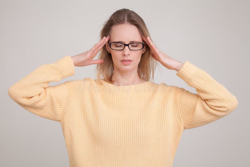 Portrait de taille- de femme blonde tenant des mains sur la t?te, ayant le mal de t?te chandail et verres jaunes de port poses co images libres de droits Portrait de taille- de femme blonde tenant des mains sur la t?te, ayant le mal de t?te chandail et verres jaunes de port poses co images libres de droits