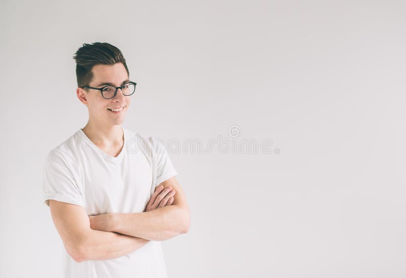 Portrait des verres de port et du T-shirt de jeune homme de ballot se tenant avec les bras croisés et sourire d'isolement sur le image stock Portrait des verres de port et du T-shirt de jeune homme de ballot se tenant avec les bras croisés et sourire d'isolement sur le image stock