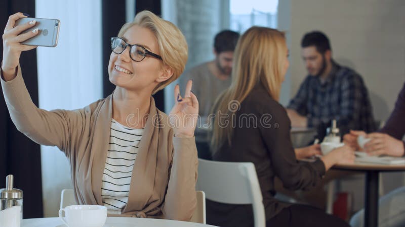 Portrait des verres de port de jeune femme élégante se reposant au café et prenant le selfie avec son téléphone intelligent photo libre de droits Portrait des verres de port de jeune femme élégante se reposant au café et prenant le selfie avec son téléphone intelligent photo libre de droits