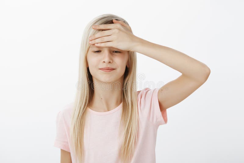 Portrait of displeased upset little girl with blond hair in pink t-shirt, holding palm on forehead and looking down with stock image Portrait of displeased upset little girl with blond hair in pink t-shirt, holding palm on forehead and looking down with stock image