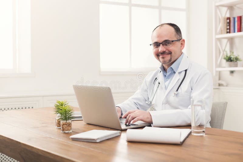 Portrait of doctor in glasses sitting at desktop stock photo Portrait of doctor in glasses sitting at desktop stock photo