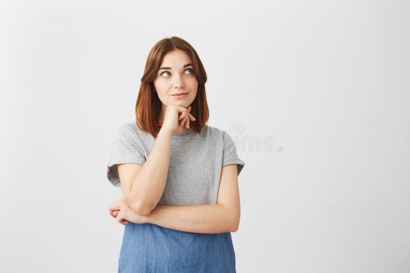 Portrait of dreamy young beautiful girl smiling looking up thinking dreaming with hand on chin over white background.