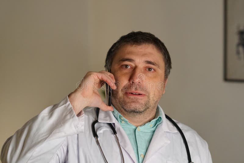 Portrait du docteur absorbé parlant à son téléphone portable image stock Portrait du docteur absorbé parlant à son téléphone portable image stock
