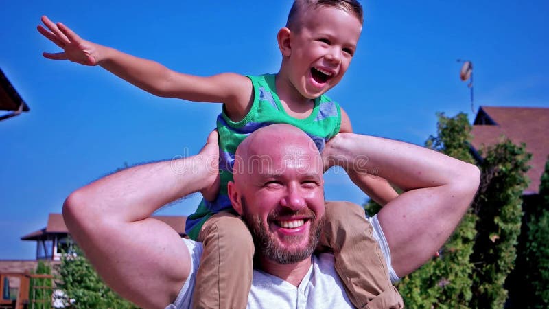 Portrait du fils et du père, enfant s'asseyant sur les épaules de sa famille heureuse de papa ayant rire d'amusement