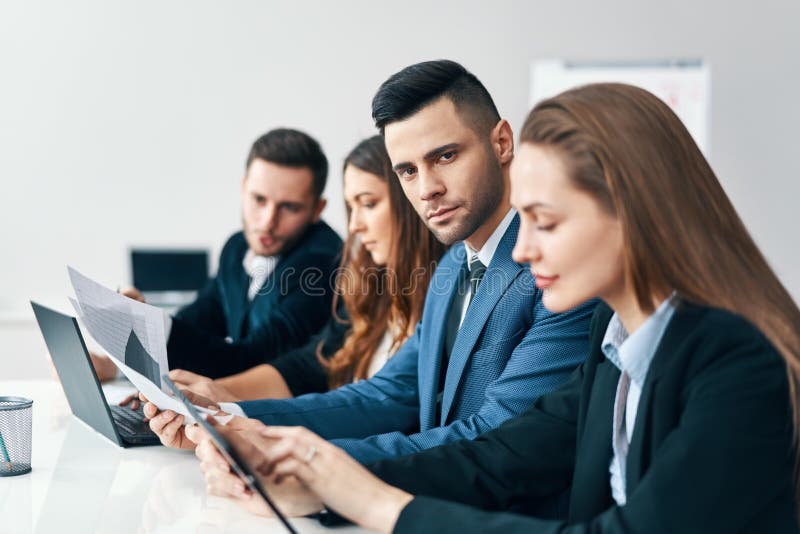 Portrait du groupe de sourire d'hommes d'affaires s'asseyant dans une rangée ensemble à la table dans un bureau moderne photo stock Portrait du groupe de sourire d'hommes d'affaires s'asseyant dans une rangée ensemble à la table dans un bureau moderne photo stock