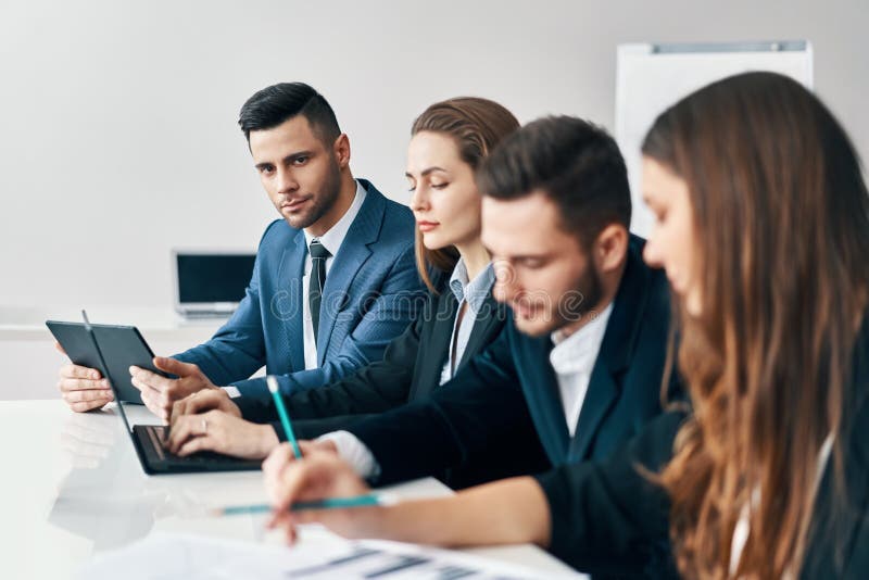 Portrait du groupe de sourire d'hommes d'affaires s'asseyant dans une rangée ensemble à la table dans un bureau moderne image libre de droits Portrait du groupe de sourire d'hommes d'affaires s'asseyant dans une rangée ensemble à la table dans un bureau moderne image libre de droits