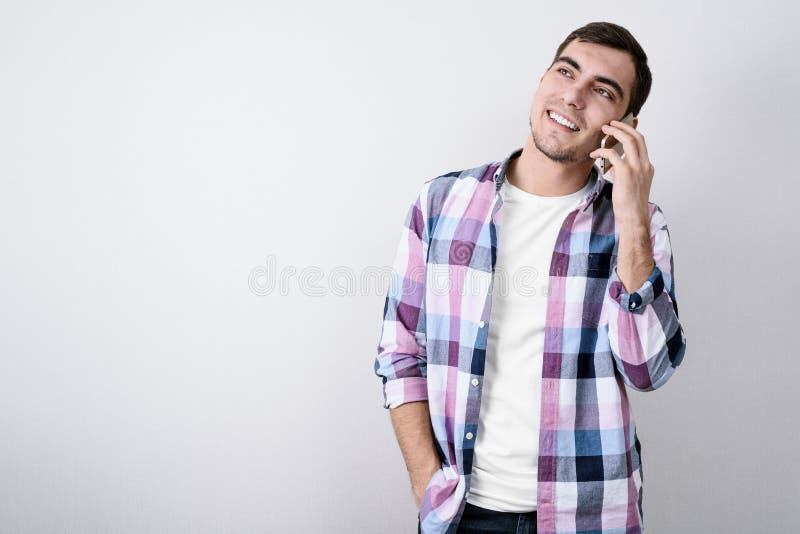 Portrait du jeune homme bel dans la chemise de plaid parlant sur le smartphone sur le fond gris avec l'espace de copie image libre de droits Portrait du jeune homme bel dans la chemise de plaid parlant sur le smartphone sur le fond gris avec l'espace de copie image libre de droits