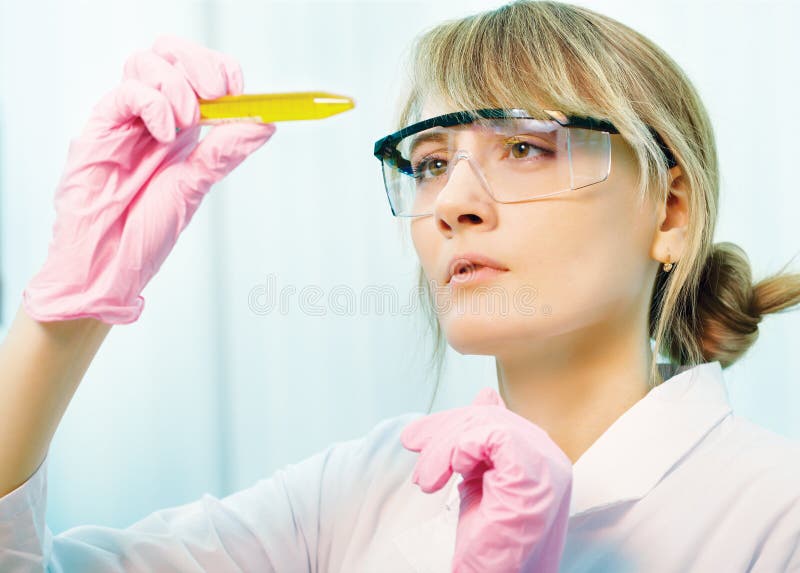 Portrait of young woman scientist in laboratory analyzing yellow liquid in test tube. Portrait of young woman scientist in laboratory analyzing yellow liquid in test tube