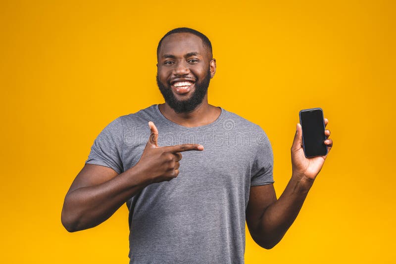 Portrait of a smiling young afro american man dressed in casual isolated on yellow background, pointing at blank screen mobile phone. Portrait of a smiling young afro american man dressed in casual isolated on yellow background, pointing at blank screen mobile phone