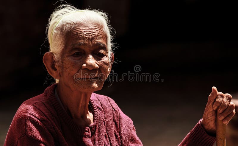 Portrait of an elderly asian woman holding walking cane on black background