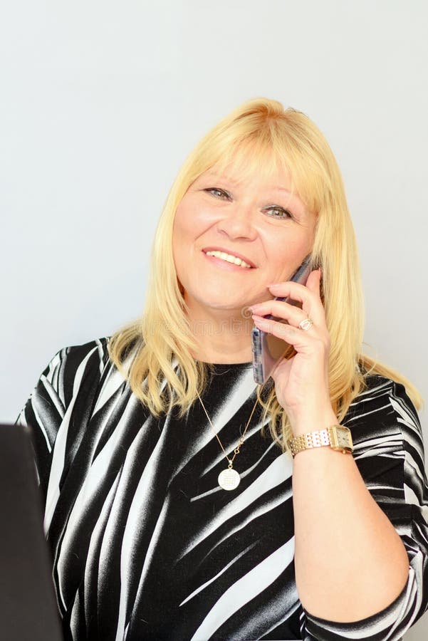 Portrait elegant middle aged plus size businesswoman talking on phone and working on laptop in creative office or cafe. stock photo Portrait elegant middle aged plus size businesswoman talking on phone and working on laptop in creative office or cafe. stock photo