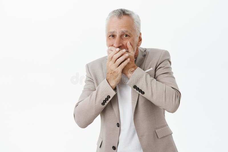 Portrait of emotive good-looking old man in elegant suit covering mouth with palms chuckling over funny fail of friend