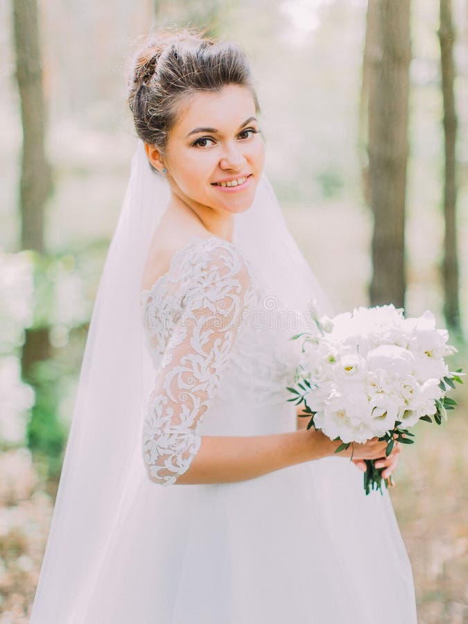 Portrait en buste de la jeune mariée gaie avec le bouquet de mariage des pivoines L'emplacement de forêt photo libre de droits