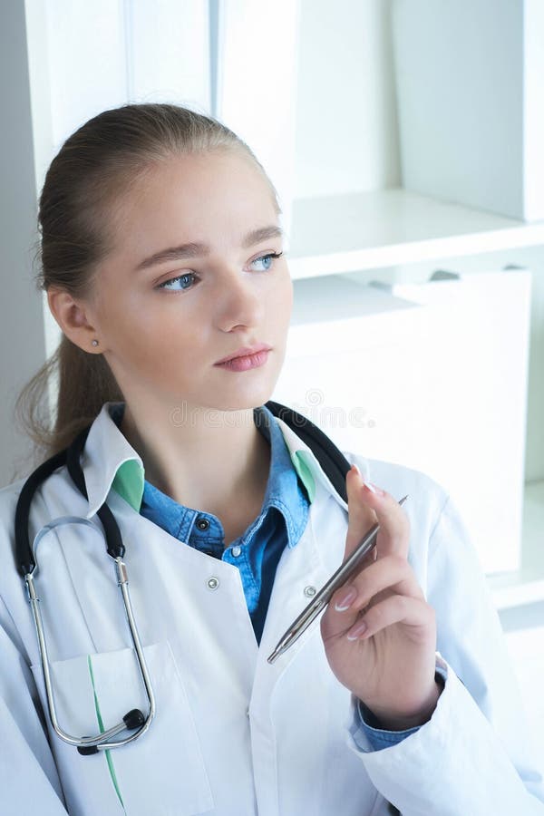 Portrait en gros plan de jeune docteur songeur dans l'uniforme blanc se reposant sur son lieu de travail Conseiller médical, infi image stock Portrait en gros plan de jeune docteur songeur dans l'uniforme blanc se reposant sur son lieu de travail Conseiller médical, infi image stock