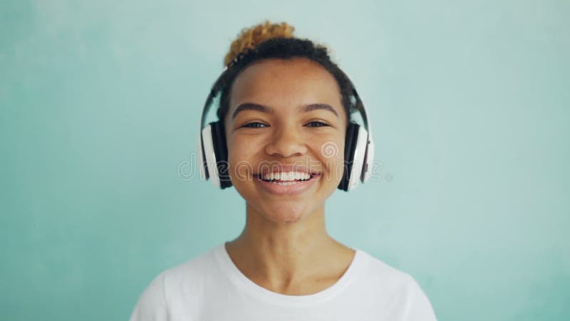 Portrait en gros plan de mouvement lent de fille heureuse d'Afro-américain dans des écouteurs regardant l'appareil-photo, le sour clips vidéos
