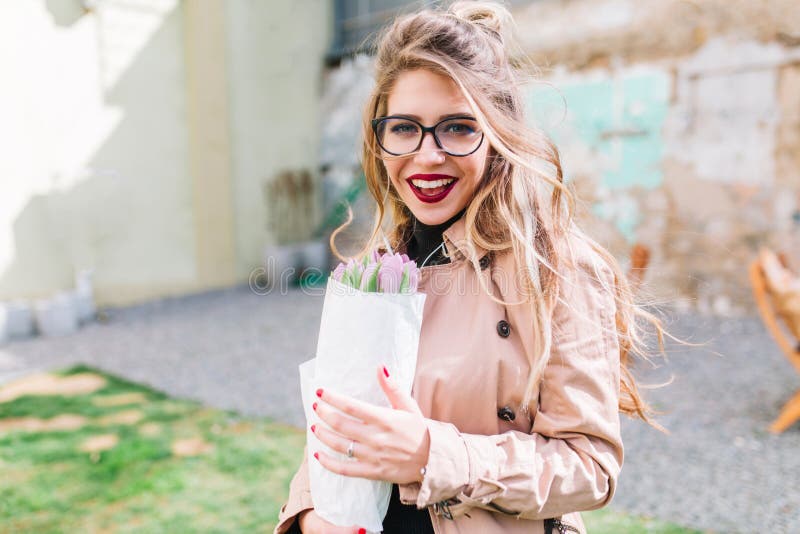 Portrait en gros plan extérieur de fille d'anniversaire tenant de belles tulipes pourpres en emballage de papier et regardant ave photo stock Portrait en gros plan extérieur de fille d'anniversaire tenant de belles tulipes pourpres en emballage de papier et regardant ave photo stock