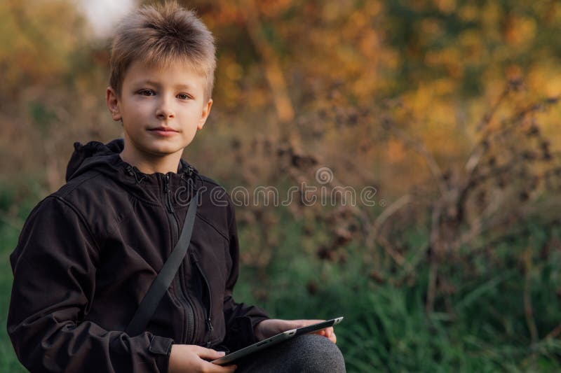 Portrait of a European blond boy in a black jacket with a tablet near a school, for online learning, a happy young man