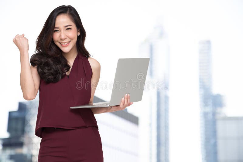 Portrait of an excited Asian woman holding laptop computer and celebrating success over building background, Raising arms with a royalty free stock images Portrait of an excited Asian woman holding laptop computer and celebrating success over building background, Raising arms with a royalty free stock images