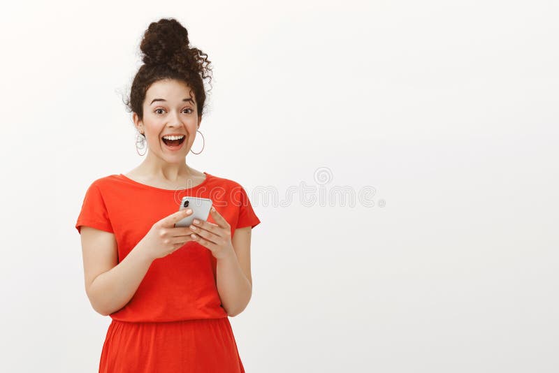Portrait of excited surprised happy girl with curly hair in red dress, holding smartphone and laughing out loud from joy royalty free stock images Portrait of excited surprised happy girl with curly hair in red dress, holding smartphone and laughing out loud from joy royalty free stock images