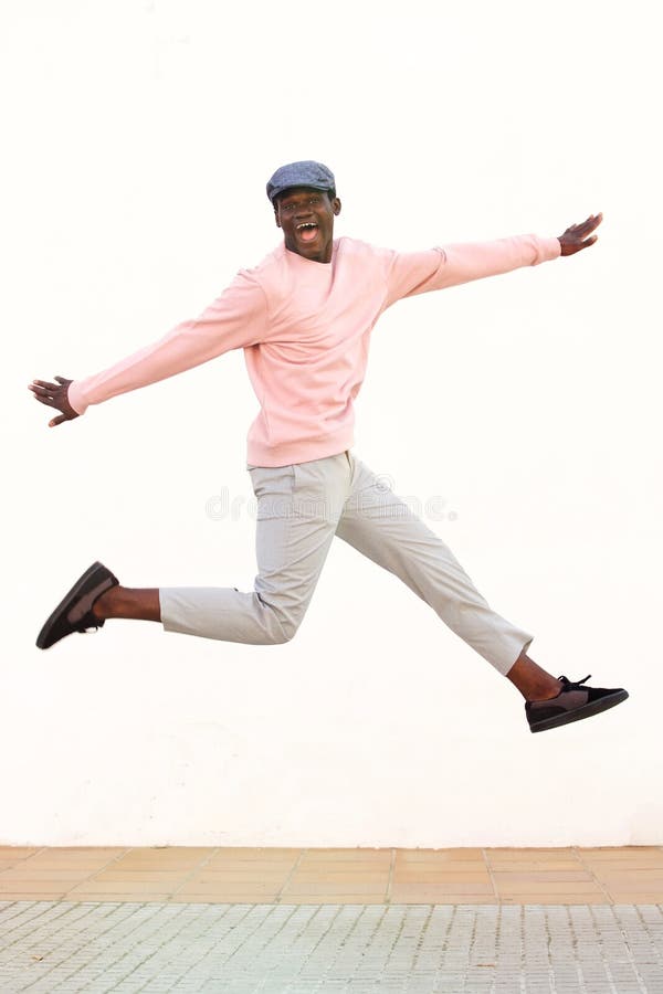Excited young african man jumping with joy against white wall