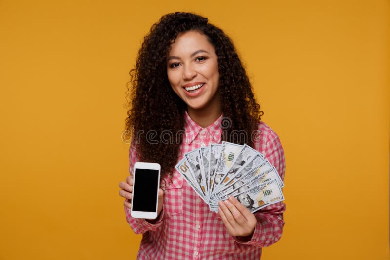Portrait of an excited young african woman holding bunch of money banknotes and looking at mobile phone over royalty free stock photo Portrait of an excited young african woman holding bunch of money banknotes and looking at mobile phone over royalty free stock photo