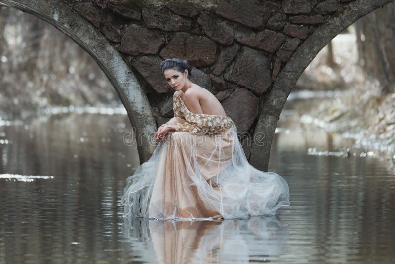 Portrait extérieur atmosphérique de jeune femme sensuelle portant la robe élégante se reposant sous le pont de la rivière photo stock Portrait extérieur atmosphérique de jeune femme sensuelle portant la robe élégante se reposant sous le pont de la rivière photo stock
