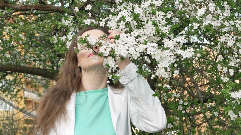 Portrait extérieur d'une belle femme dans la veste blanche parmi l'arbre blanc de fleur banque de vidéos Portrait extérieur d'une belle femme dans la veste blanche parmi l'arbre blanc de fleur banque de vidéos
