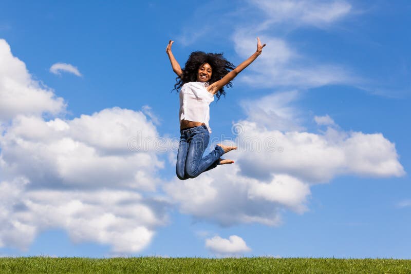 Portrait extérieur d'une fille noire adolescente sautant par-dessus un ciel bleu
