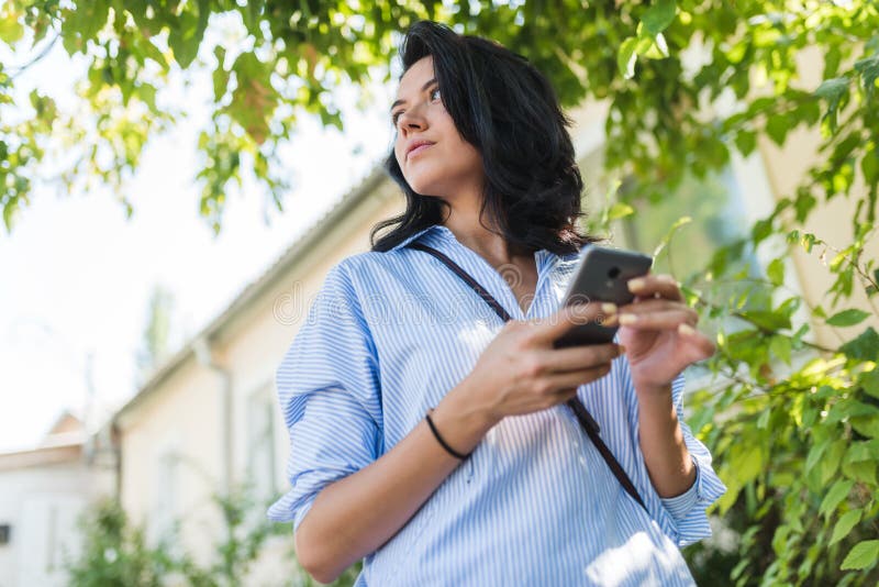 Portrait extérieur de belle brune femelle dans des vêtements sport dans la rue utilisant le téléphone portable, regardant de côté photo libre de droits Portrait extérieur de belle brune femelle dans des vêtements sport dans la rue utilisant le téléphone portable, regardant de côté photo libre de droits