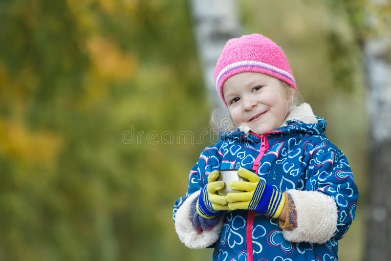 Portrait extérieur principal de chute et d'épaules de petite fille tenant la tasse en acier de flacon de thermos dans des mains photo stock