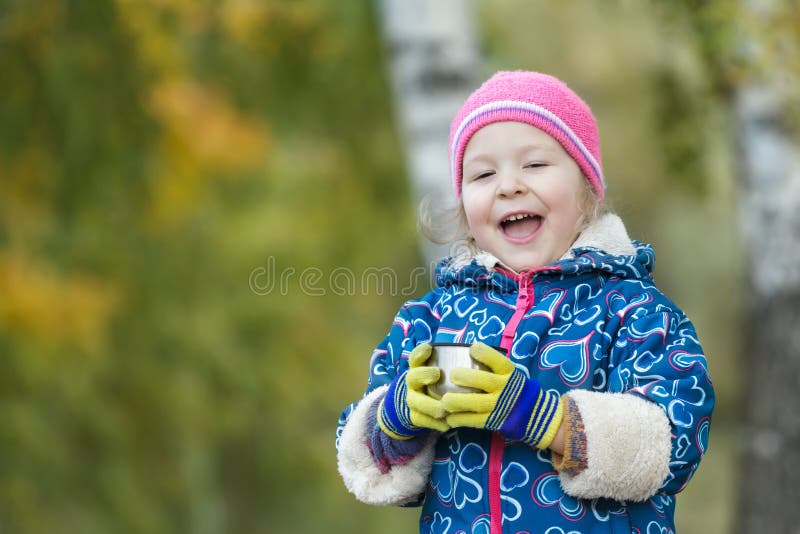 Portrait extérieur saisonnier principal et d'épaules de petite fille tenant la tasse en acier de flacon de thermos dans des mains photos libres de droits