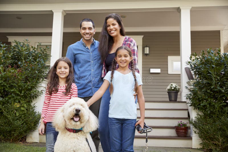 Portrait Of Family Standing in Front Of House With Pet Dog