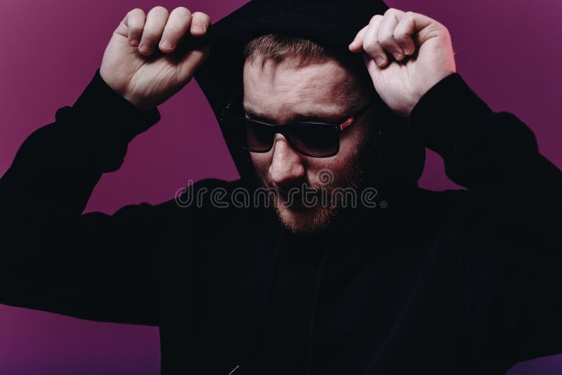 Portrait of fashion man in a black sweater with a hood and sunglasses in neon light in the studio royalty free stock photography Portrait of fashion man in a black sweater with a hood and sunglasses in neon light in the studio royalty free stock photography