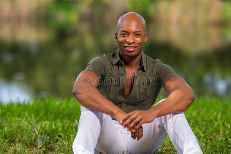 Portrait fashionable African American man sitting on grass in the park. Man is smiling and looking at camera stock photography Portrait fashionable African American man sitting on grass in the park. Man is smiling and looking at camera stock photography