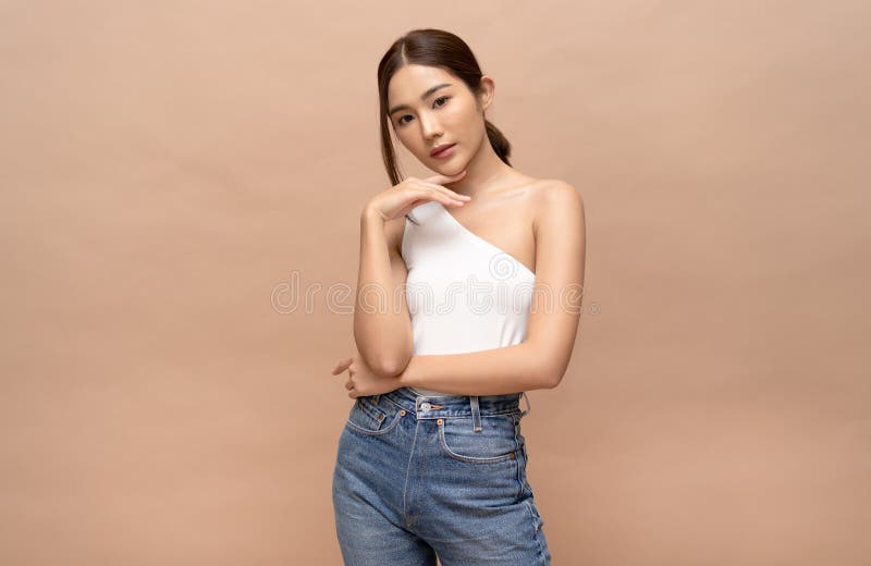 Portrait of fashionable beautiful young sexy Asian woman with natural make-up and looking at camera standing near white wall. Lady