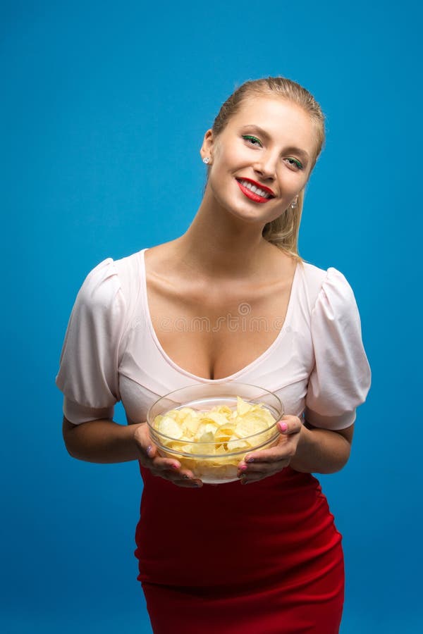 Portrait of fashionable young blond woman in pink-red dress, bright make-up holding, eating fried potato, chips and over stock photography Portrait of fashionable young blond woman in pink-red dress, bright make-up holding, eating fried potato, chips and over stock photography