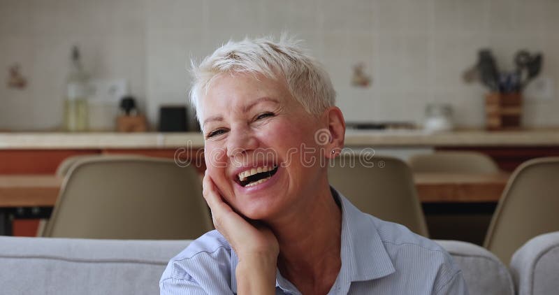 Portrait femme âgée heureuse assise sur un canapé pose à la caméra banque de vidéos
