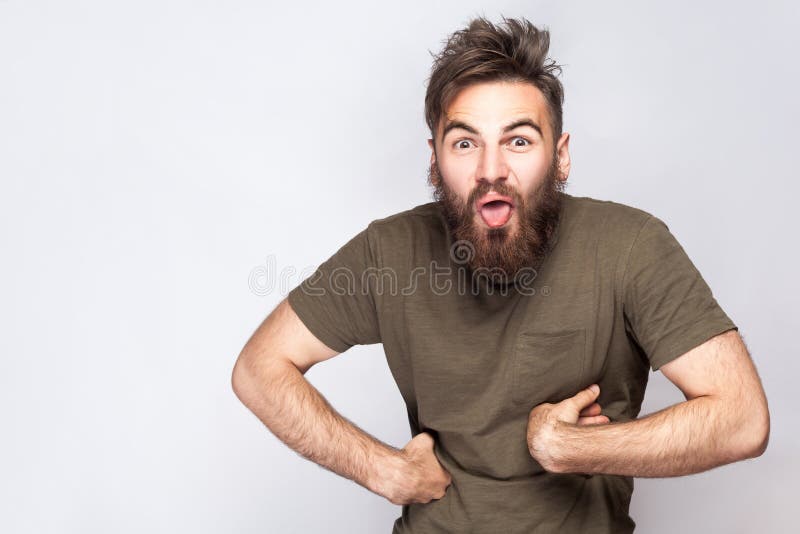 Portrait of funny crazy bearded man with tongue out and dark green t shirt against light gray background. royalty free stock photos