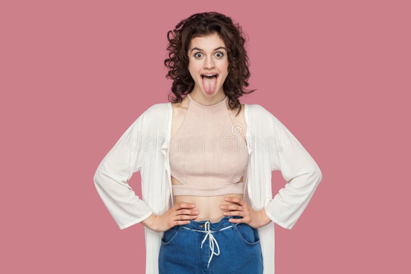 Portrait of funny crazy beautiful brunette young woman with curly hairstyle in casual style standing, hands on waist and tongue stock images